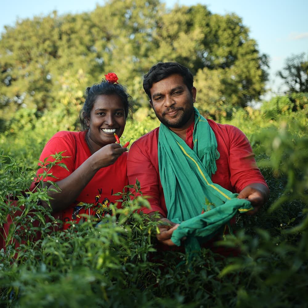 Smiling pair in a green farming landscape.